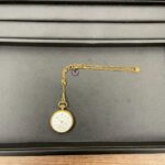 「蒔田店で査定したウォルサムの18金懐中時計。金チェーンと紫色ストーン付きのヴィンテージ品が黒い査定トレーに置かれた写真。」