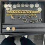 黒いトレーに18金ブレスレット、金チェーン、シルバーリング、古銭や銀貨が並んでいる写真。蒔田店で金アクセサリーやシルバー・古銭をまとめて買取している様子。