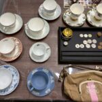 ブランド食器のカップ＆ソーサーやコイン、コーチのバッグがテーブルに並んでいる様子（ウェッジウッド・ロイヤルコペンハーゲンなど）