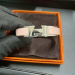 黒い手袋をしたスタッフが、ピンク×シルバー金具のHERMÈSクリッククラックHブレスレットを箱に入れて持っている写真。エルメスアクセサリーの査定イメージ。