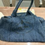テーブルの上に置かれたPRADAカナパのデニムトートバッグの写真。伊勢佐木モール本店でプラダのバッグを査定している様子。
