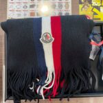 黒・白・赤のトリコロールカラーのMONCLERマフラーが査定トレーの上に置かれている写真。蒔田店でモンクレールのマフラー買取を行っているイメージ。