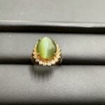 キャッツアイとダイヤモンドを組み合わせたゴールド枠のリングを黒い台の上に置いた買取実績写真